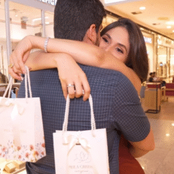 Sacolas personalizadas da marca Paula Cristina Semijoias, em tom claro com estampa floral delicada e acabamento sofisticado com alças de cordão branco e laço de fita.